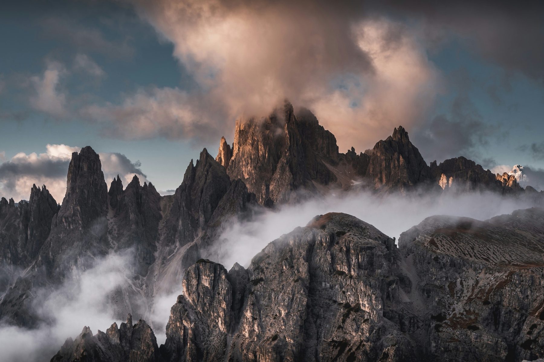 Jagged rock spires of the Cadini di Misurina rising through mist, with glowing clouds above