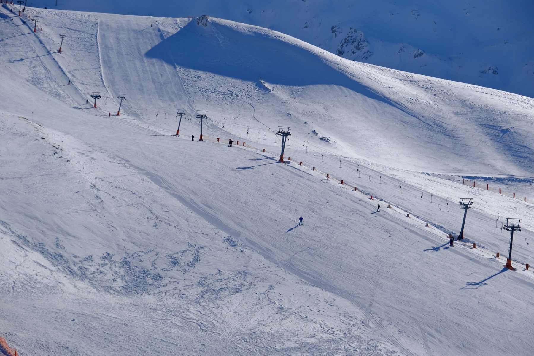 A wide groomed slope with a drag lift and a few skiers