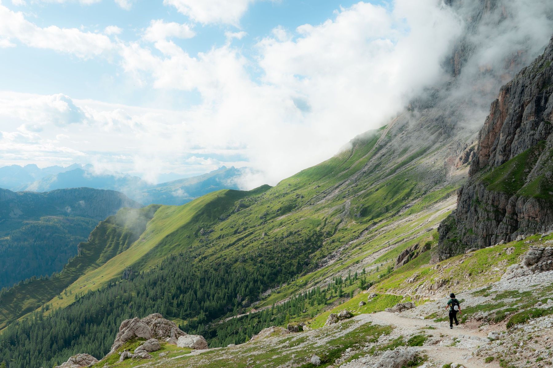 A hiker on a trail across a green mountain slope