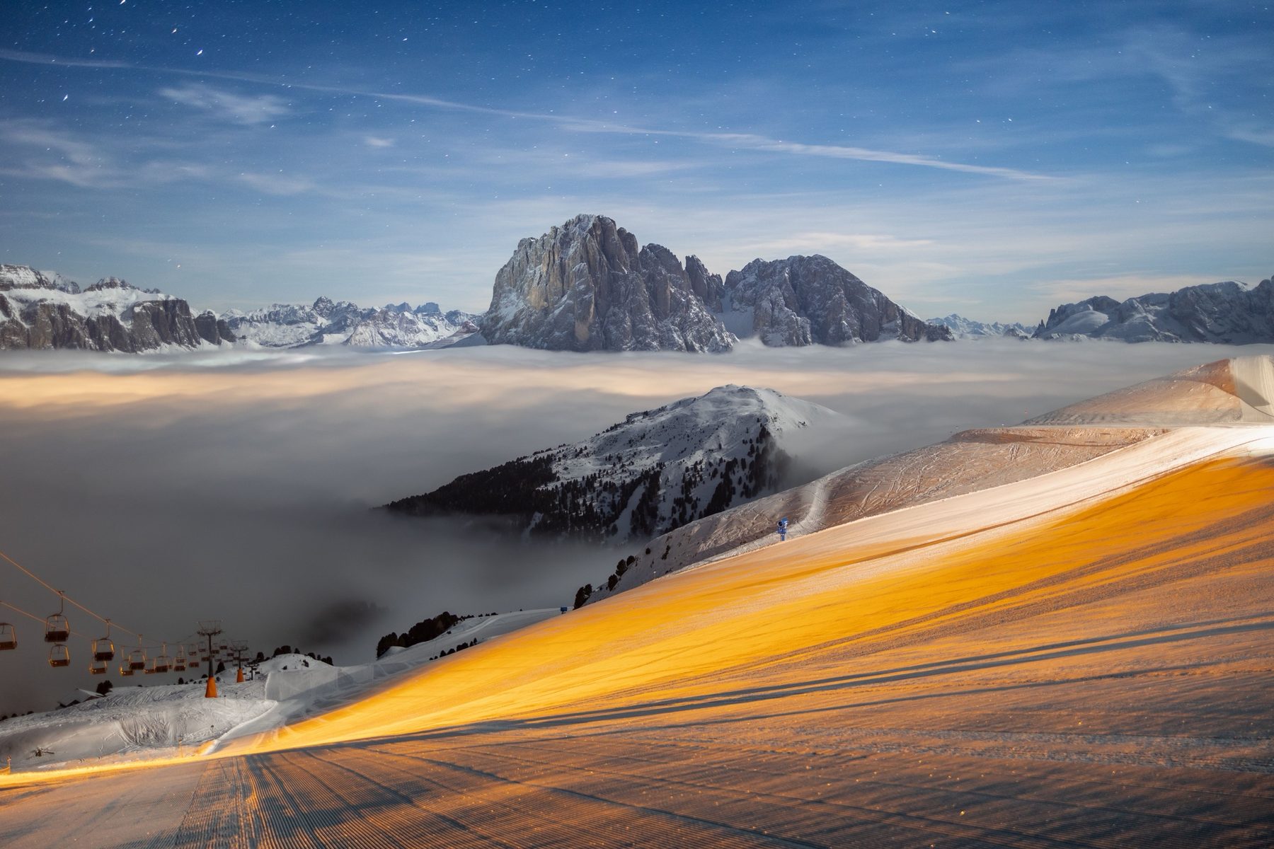 A freshly groomed piste and chairlift below the Sassolungo at night