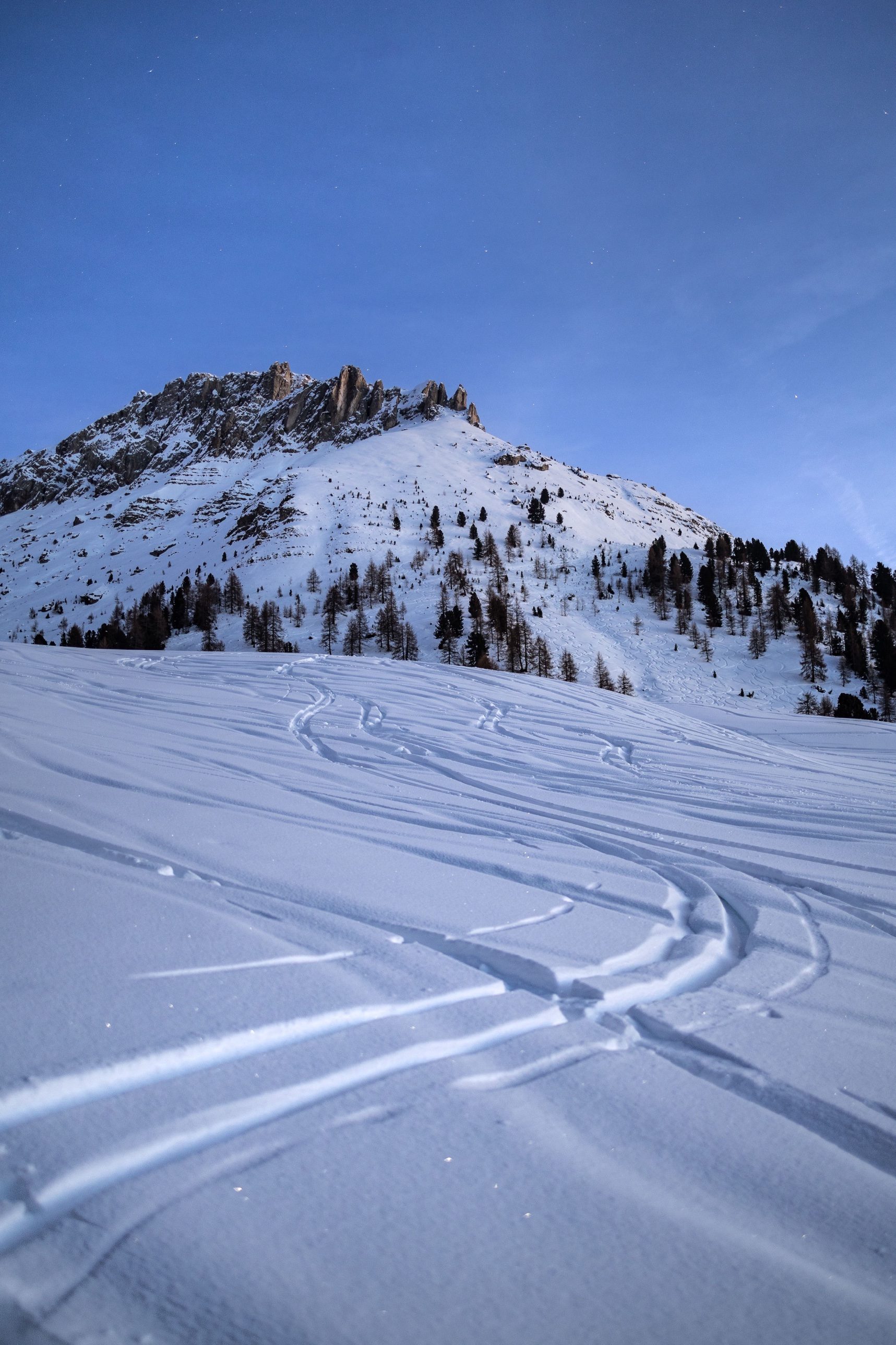 Ski tracks in fresh snow below a rocky ridge at dusk