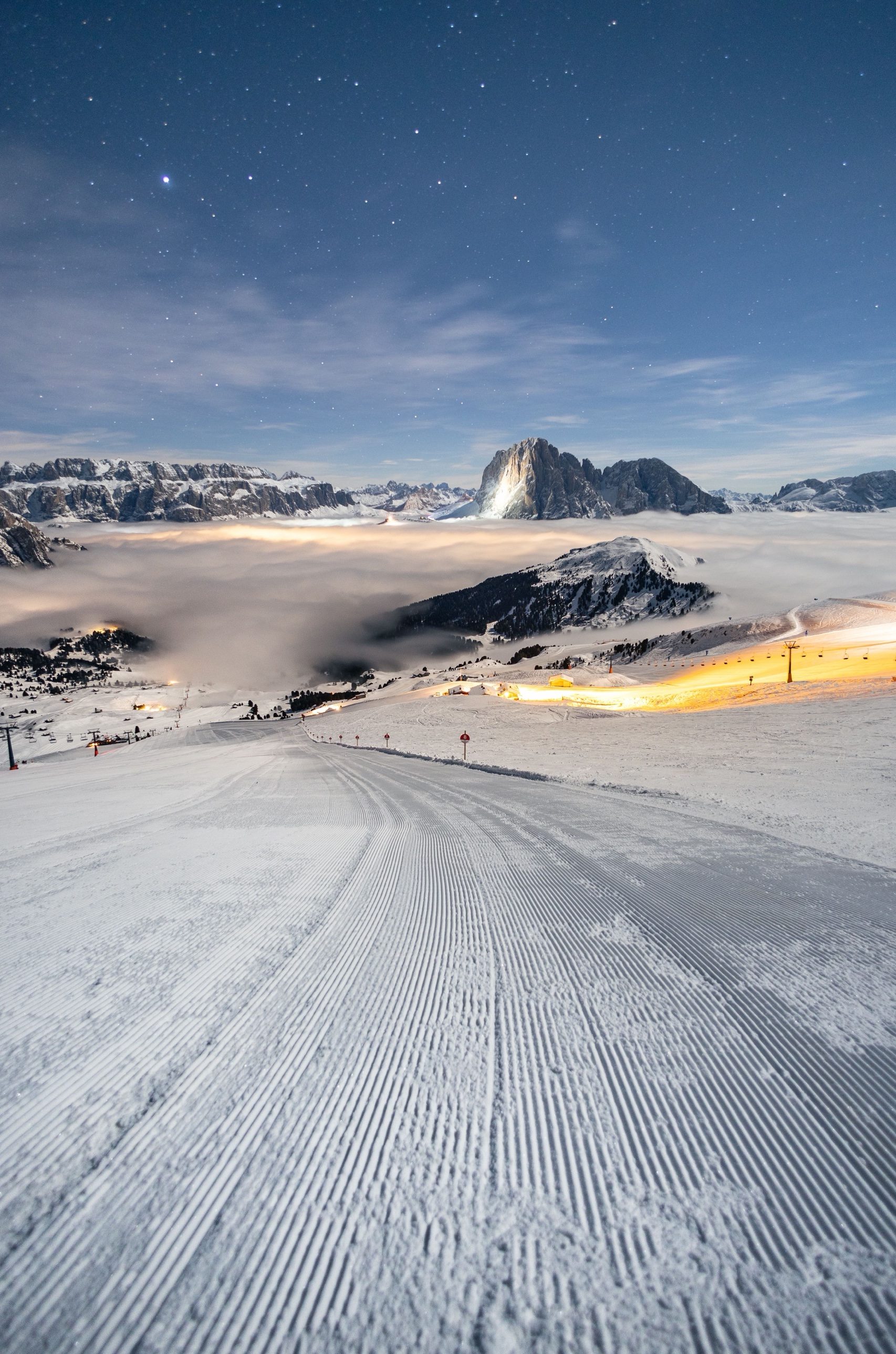 A freshly groomed piste at night with the Sassolungo and the Sella group behind