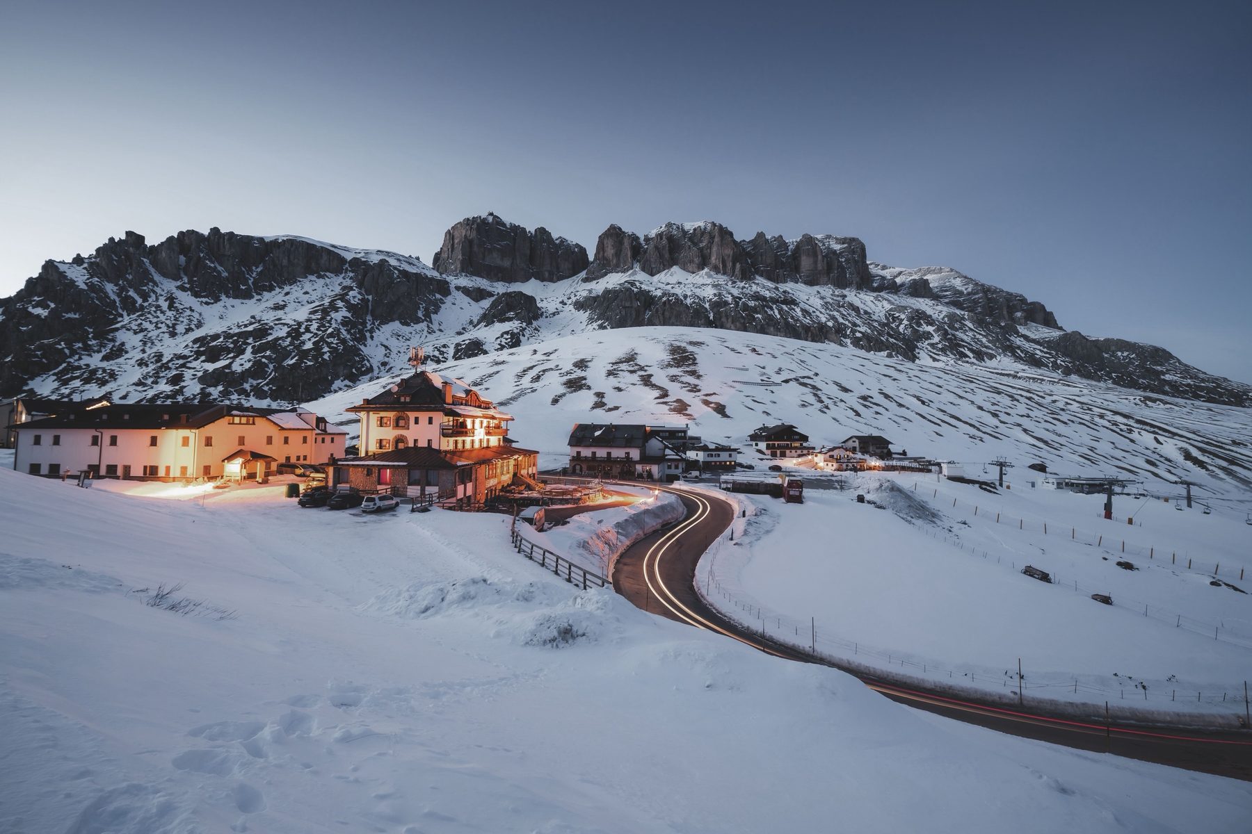 Hotels and a winding road at Passo Pordoi at dusk below the Sella walls