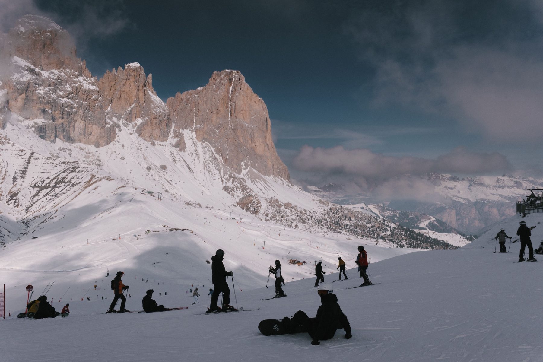 Skiers and a snowboarder on a piste below the Sassolungo