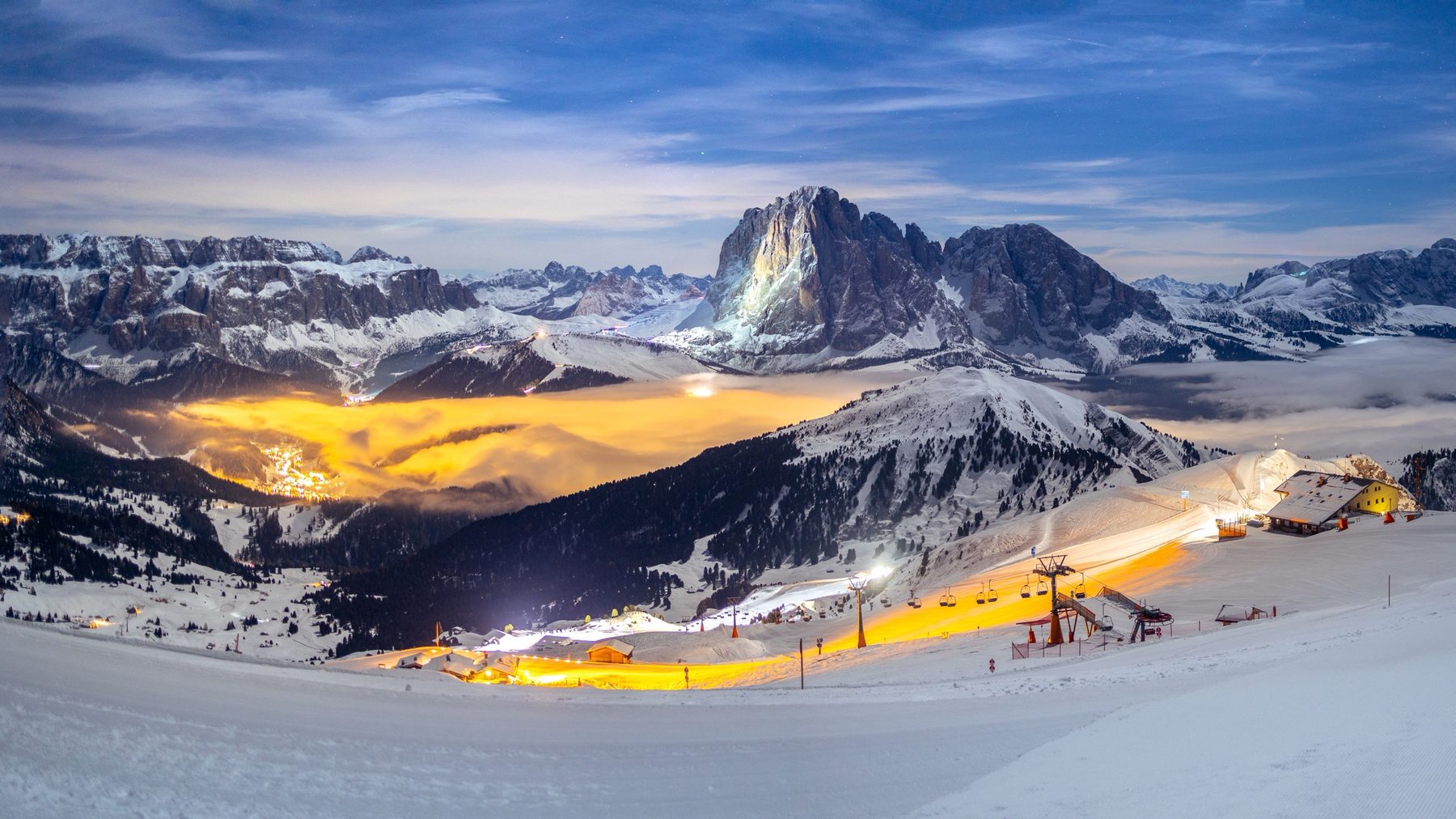Val Gardena at night, its villages glowing under cloud below the Sassolungo and the Sella group